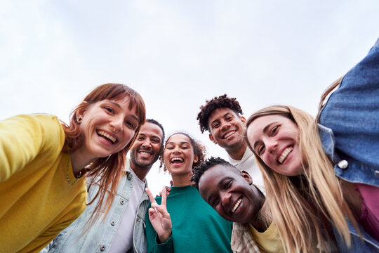 Copy space image of a multicultural group of friends gathering outdoors, taking a selfie, looking camera cheerfully. Low angle view.
