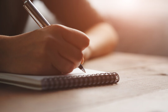 Young woman writing with pen on notebook at sunset, diary and memo notes