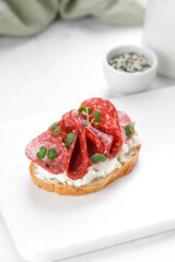 Sandwich, toast with cream cheese, sliced salami, sausage, microgreen on white cutting board. Snack, bruschetta.