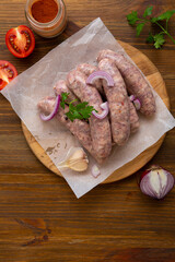 Several of uncooked bbq sausage on wooden board with spice onion tomato