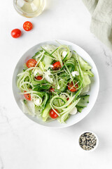 Healthy green fresh salad with sliced cucumber, tomatoes, mozzarella cheese, diet dinner concept. Cucumber salad on white plate. Top view.