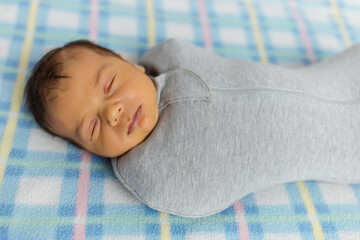 The baby is lying in a cocoon on cot. He sleeps sweetly and dreams.