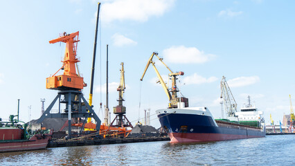Vessel on which coal is loaded at seaport. Port cranes for loading coal onto ship, Kaliningrad, Russia. Coal on pier at seaport. Preparation for loading coal on ship