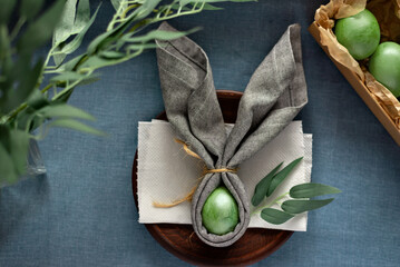 Aesthetic Easter table decoration, banny ears napkin and green dyed eggs on blue background, spring...