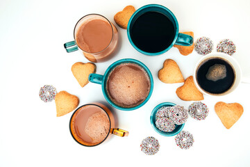 Mugs of coffee with foam and a plate with heart-shaped shortbread cookies on a white background. Top view