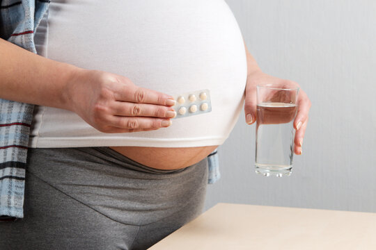 A Pregnant Girl Holds Pills And A Glass Of Water. Concept, Taking A Large Number Of Medications During Pregnancy.