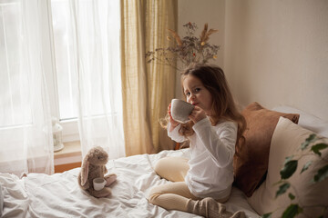 Curly-haired little blue-eyed girl of 4 plays with her plush rabbit in tea party. Children's room....