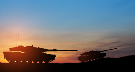 Fototapeta na wymiar Silhouettes of army tanks at sunset sky background. Military machinery.