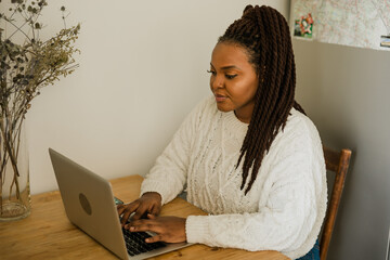 Portrait african american woman using laptop while sitting on chair in living room - student, video...