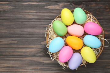 Colorful easter eggs in basket on dark brown wooden background. Top view