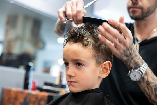 Hairdresser combing and cutting a boy's hair in his barbershop. Hairdressing and childhood concept.