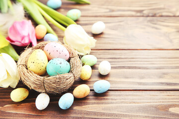Colorful eggs in nest and flowers tulips on brown wooden background