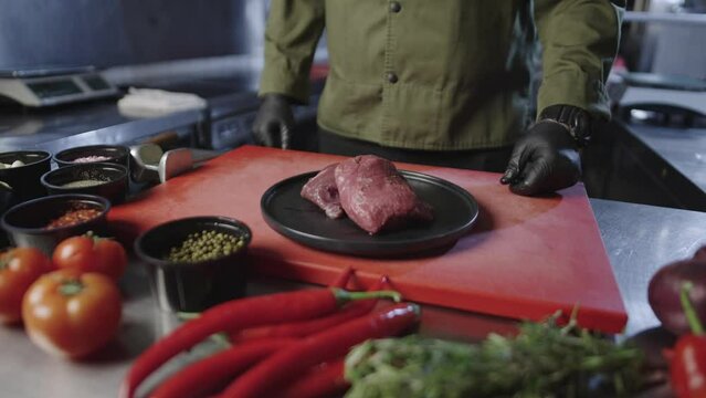The chef puts a plate of juicy meat on the cutting board. On the table there are all the ingredients for preparing a delicious stava. Use of natural products. High quality 4k footage