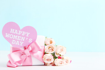 Bouquet of roses, gift and card in shape with text Happy Women's Day on blue background