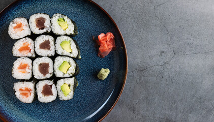 Set of different types of sushi rolls with salmon, tuna and avocado. On rustic background with space for text