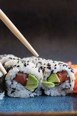 A set of fresh sushi rolls with salmon, avocado and sesame seeds with chopsticks