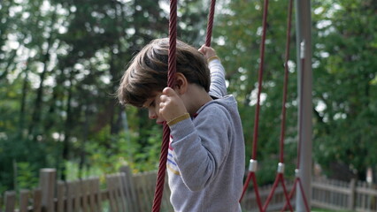 Active child keeping balance at playground structure with ropes. One playful little boy playing outdoors at park during sunny autumn day