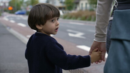 Child holding mother hands waiting to cross street at crosswalk. Family trust concept. Parent and kid hand held together