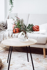 Vase with protea flowers on coffee table indoors and sofa with pillows, space for text. Scandinavian interior design elements