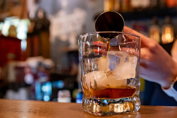 woman hand bartender making negroni cocktail. Negroni classic cocktail and gin short drink with sweet vermouth, red bitter liqueur in bar