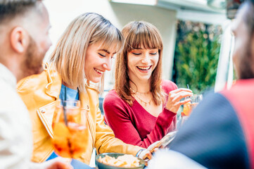 People drinking spritz at in backyard of cocktail bar restaurant - Two girls smiling together - Lifestyle concept with young friends having fun together drinking during happy hour at pub.