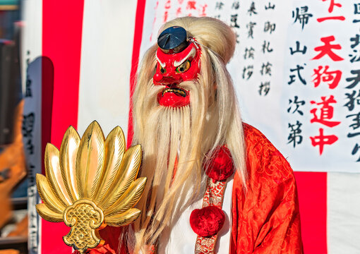tokyo, setagaya - january 28 2023: Japanese man dressed in Suzukake kimono wearing a Tokin headwear and a bearded red mask of Tengu holding a golden fan during the Shimokitazawa parade festival.
