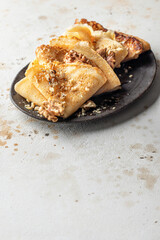Crepes with honey or syrup and nuts on brown plate on beige textured background with copy space. Pancake day or Maslenitsa traditional food concept