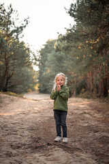 Fototapeta premium Little blonde girl dancing jumping on the sand in a pine forest
