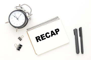 On the black and white flat lay, a pen and notebook with the word RECAP. Business concept