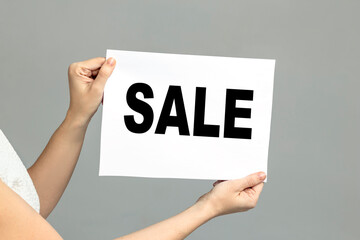 Female hand holds a piece of paper with the inscription sale over graybackground cardboard with sale written on to promote special sales