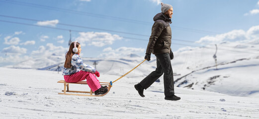 Man pulling a girl with a wooden sleigh on a mountain hill