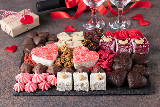 Charcuterie sweet board with different sweets, chocolate, marmalade hearts, nuts and candies as well wine and two glass on brown background. Snacks dessert for romantic Valentines Day