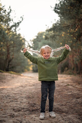 Little blonde girl dancing jumping on the sand in a pine forest