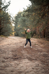 Little blonde girl dancing jumping on the sand in a pine forest