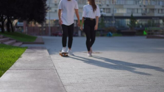 Blurred young couple riding skateboard walking on city street in slow motion passing camera leaving. Unrecognizable confident millennial Caucasian man and woman strolling outdoors enjoying leisure