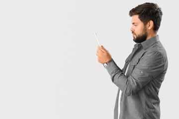 Handsome young businessman using tablet computer on light background