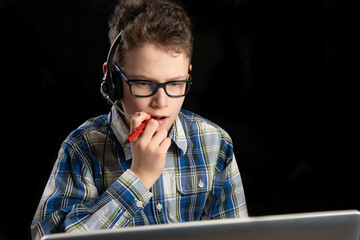Boy in shirt and glasses nervously chews on his pen in front of the laptop while doing his homework...