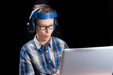 Boy frontal with headband and headphones in front of the laptop makes an astonished face at his homework studying at home