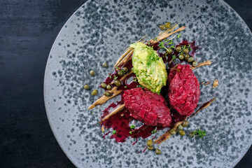 Modern style gourmet tartar raw from chianina beef filet with avocado and capers in amareno cherry and truffle sauce served as top view on a Nordic design plate