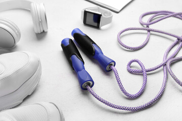 Skipping rope with smartwatch, headphones and sneakers on white background, closeup