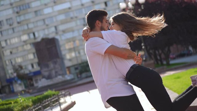 Loving happy young man spinning smiling woman in slow motion as live camera tilting. Portrait of positive carefree excited Caucasian couple having fun dating outdoors on sunny spring summer day