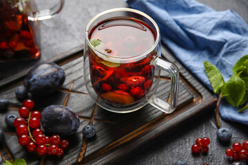 Board with glass cup of fruit tea and berries on dark background, closeup