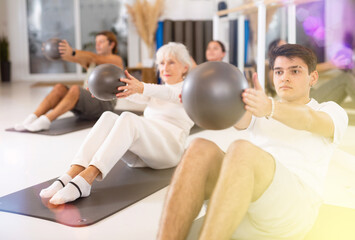 Fototapeta premium Sporty energetic males and females doing exercises with pilates ball during group training at gym. Fitness concept.