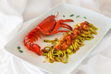 Green tagliolini with lobster on white plate, dish / gourmet cuisine.