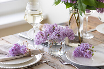 Obraz na płótnie Canvas Beautiful table decor for a wedding dinner with a spring blooming lilac flowers. Celebration of a special event. Fancy white plates, wineglasses. Countryside style