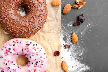 Sheet of baking paper with tasty donuts and nuts on dark background, closeup