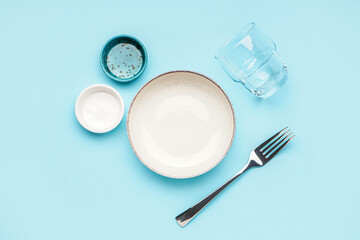 Clean dishware and fork on blue background