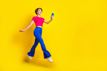 Fototapeta na wymiar Full length photo of positive cute lady user walk empty space speaking modern device gadget isolated on yellow color background
