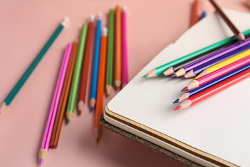 Notebook with colorful pencils on pink table, closeup