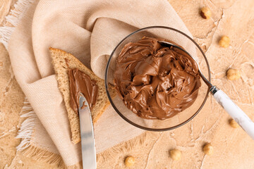 Bowl of tasty hazelnut butter and toast on color background